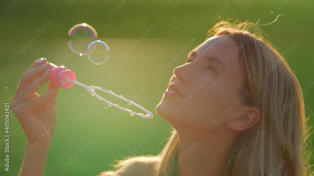 Portrait of beautiful woman blowing soap bubbles in city park at summer evening.