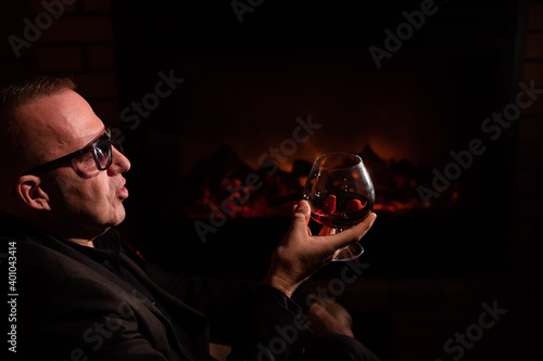 Mature man drinking cognac by the fireplace.