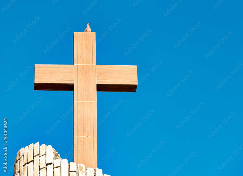 Christian cross symbol on top of a church in a blue sky daytime. There is a dove perching on top