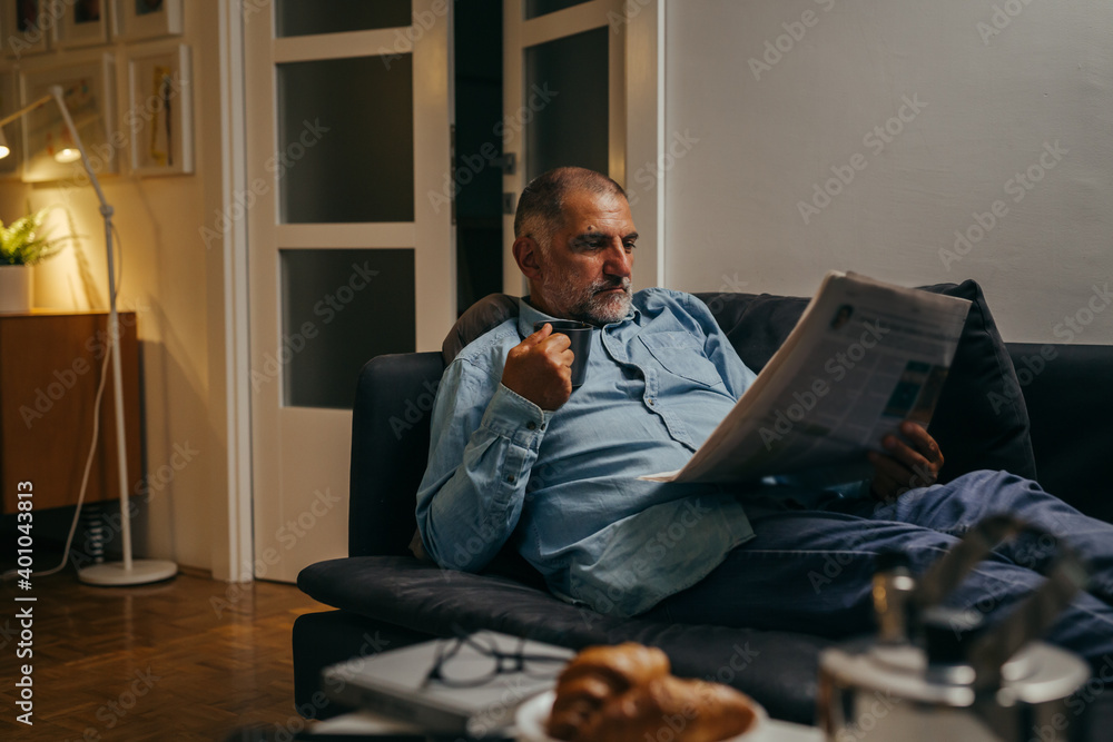 Fototapeta premium man laying on sofa and reading newspapers at his home
