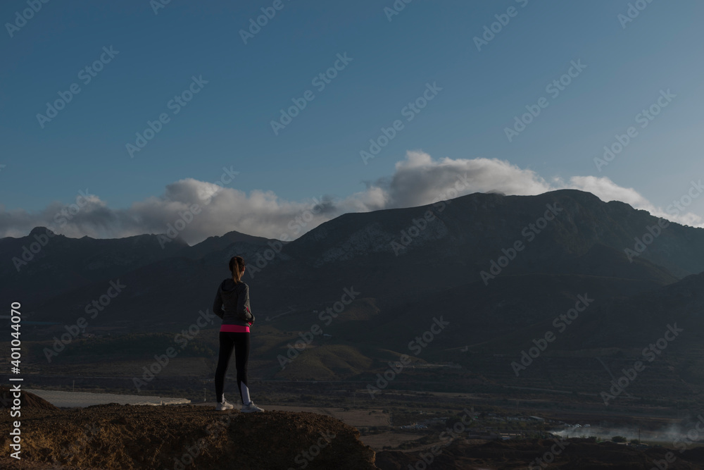 Back view of woman standing on a mountain with view of clouds and mountains on background