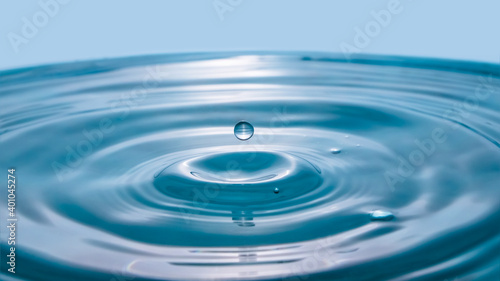 Water drop on blue background. Blue water surface with splash. Clear Waterdrop with circular waves. Splashes closeup. Water splash and falling drop. Splash of the falling drops of water.