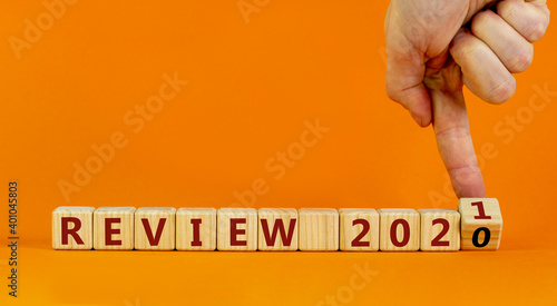 Symbol of 2021 new year review. Male hand flips a wooden cube and changes words 'Review 2020' to 'Review 2021'. Beautiful orange background, copy space. Business and 2021 review concept.