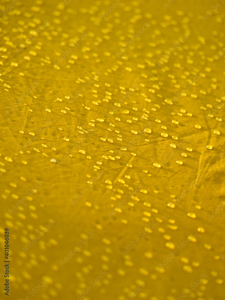 Water drops on waterproof membrane fabric. Detail view of texture of yellow synthetic waterproof cloth. Morning dew on tent. Water drops on waterproof membrane fabric. Detail view of texture of yellow synthetic waterproof cloth. Morning dew on tent.
