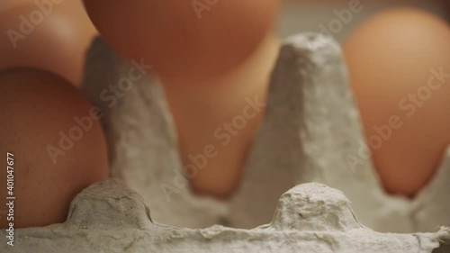 Cooking food, healthy food. A man's hand takes chicken eggs from a cardboard tray. Brown chicken eggs in a tray on a brown background, close-up, side view. Slider shot 4K UHD