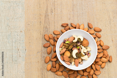 A variety of nuts and bean are in a bowl on the wooden background at the right of the image, top view, flat lay, top-down.