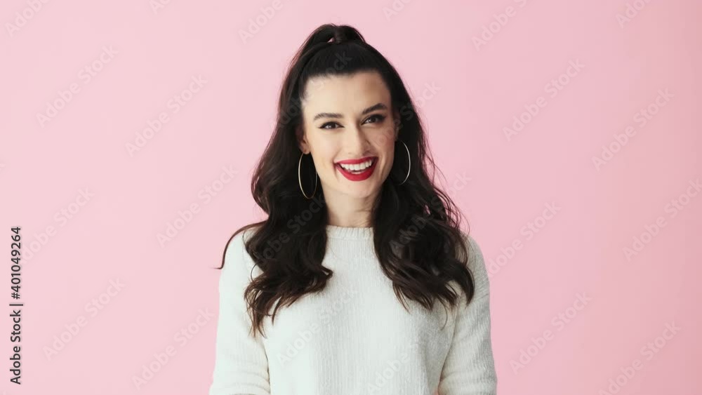 A pretty nice woman with red lips is nodding while looking to the camera standing isolated over pink background in studio A pretty nice woman with red lips is nodding while looking to the camera standing isolated over pink background in studio