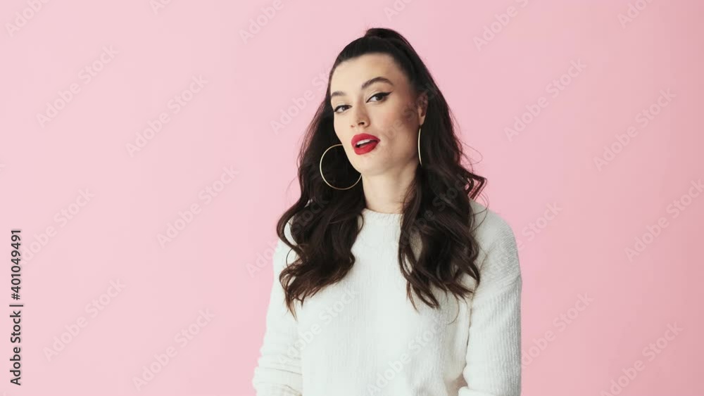 A displeased woman with red lips is feeling bored standing isolated over pink background in studio A displeased woman with red lips is feeling bored standing isolated over pink background in studio