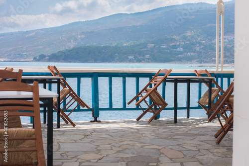 Fototapeta Naklejka Na Ścianę i Meble -  Cafe on the terrace overlooking the sea. Ikaria island, Greece. Superb summer mood, outdoor restaurant. Romantic vibes, summer colors under white tent and blue sky.