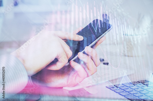 Double exposure of man's hands holding and using a digital device and forex graph drawing. Financial market concept.