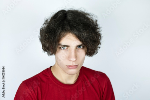 Portrait of a handsome teenage boy on a light background, the boy has rather long curly hair and a sad face, the guy misses his childhood © Мар'ян Філь