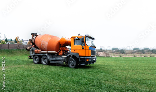 A large orange concrete mixer has arrived at the construction site. Special equipment transport for the delivery of building material - ready mixing cement. Business card, banner with copy space