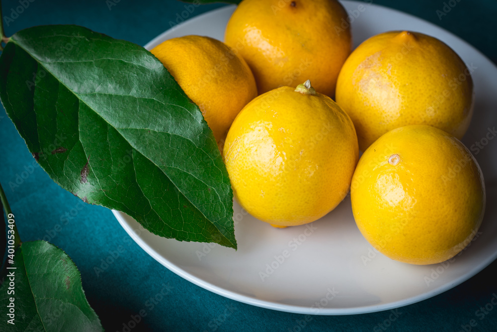 Persian Sweet lemons (Citrus limetta) on a white plate, green leaves and blue turquoise table 
