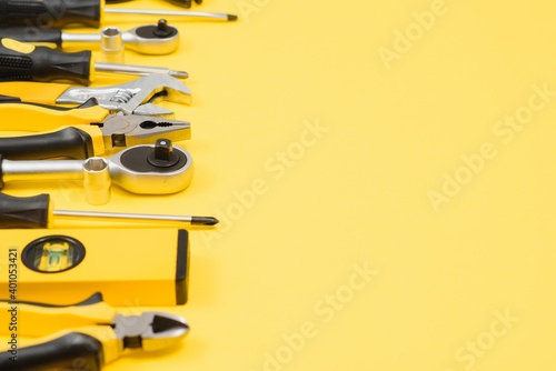 Yellow and black handy tools (pilers and screwdriver) isolated on yellow background