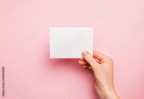 Hand with white blank card on pink background. Copy space, space for text. Mockup template for design.