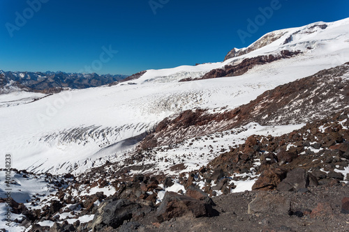 Rocks and white slopes of Elbrus, Caucasus. Snow-covered peaks and clear blue skies. Winter mountains, alpine skiing. Sunny snowy landscape. Panoramic mountain view.