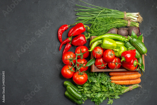 Vegetable basket with a bunch of green and peppers cucumber and tomatoes with stem carrots beets on dark background