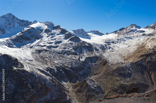 Snow-capped peaks and clear blue skies. Winter mountains, alpine skiing. Sunny snowy landscape. Panoramic mountain view. Rocks and white slopes covered with glaciers