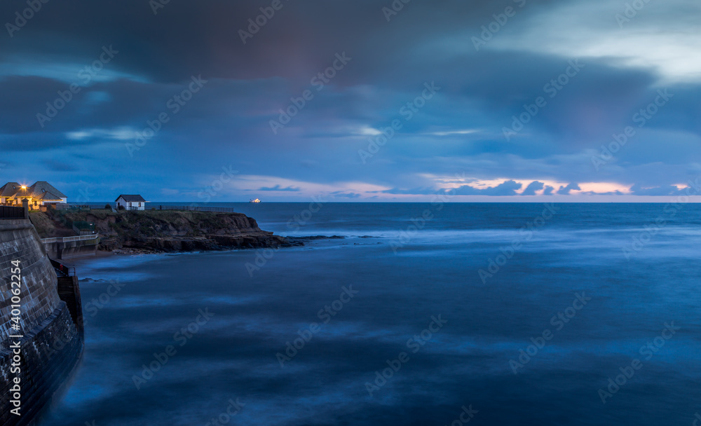 A white house on the cliffs in Cullercoats during Blue hour with clouds over-head