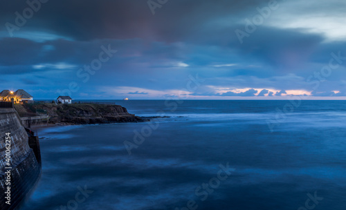 A white house on the cliffs in Cullercoats during Blue hour with clouds over-head