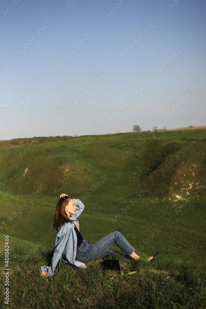 Young woman is sitting on green grass hills and feeling relax on summer sunny day