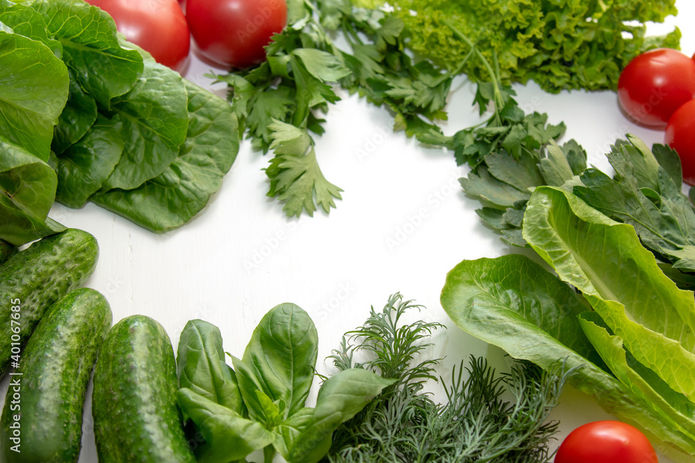 Fresh vegetables tomatoes, cucumbers, parsley, dill, basil and green leaves for salad on a white table. Fresh vegetables tomatoes, cucumbers, parsley, dill, basil and green leaves for salad on a white table.