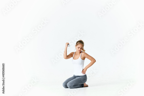 woman with dumbbells and in sportswear sits on the floor in a bright room