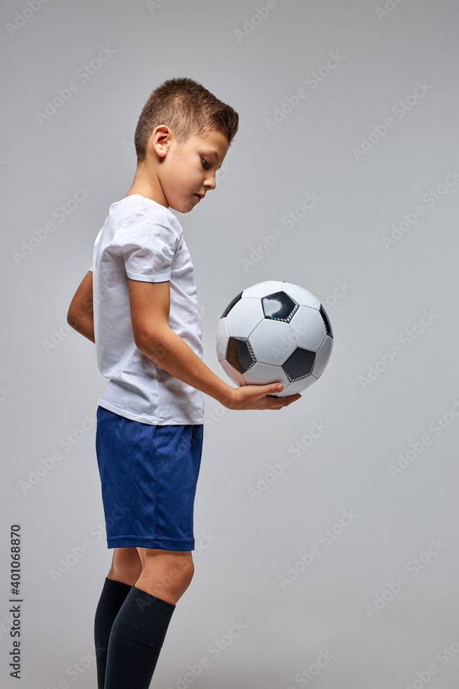 young boy in sportswear holding soccer ball, posing at studio. athletic child enjoy sportive games. football concept. side view