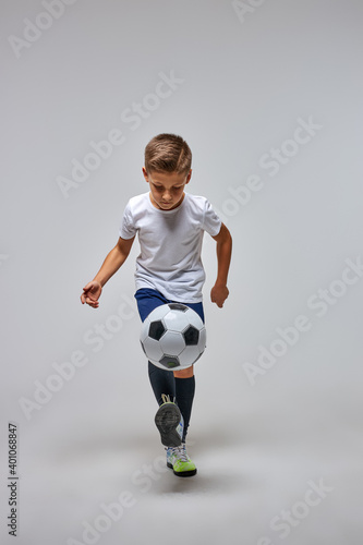 boy kicking soccer ball by knee isolated on gray, do training exercises alone
