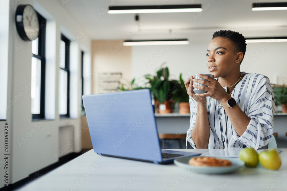 Thoughtful young businesswoman drinking coffee at laptop in office Thoughtful young businesswoman drinking coffee at laptop in office