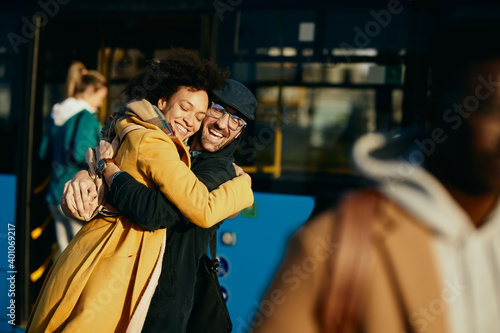 Happy couple embracing with eyes closed while meeting at bus station.
