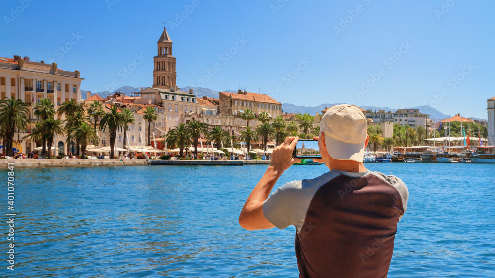 View of a tourist with a smartphone taking pictures of the promenade the Old Town of Split with the Palace of Diocletian and bell tower of the Cathedral of Saint Domnius, the Adriatic coast of Croatia