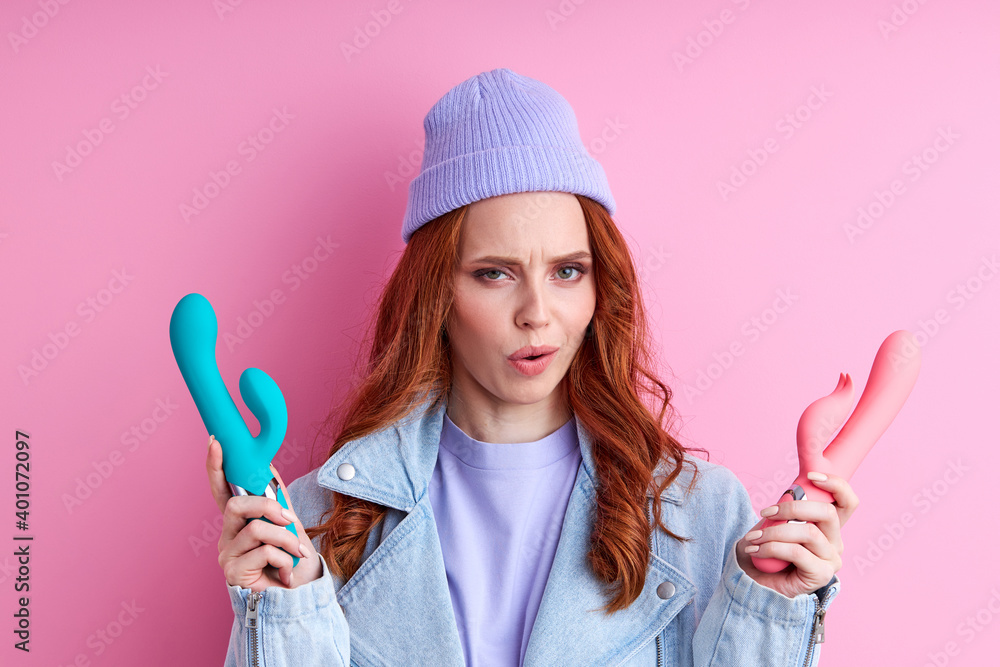 woman is misunderstanding how to use vibrators , have fun posing at camera isolated on pink background woman is misunderstanding how to use vibrators , have fun posing at camera isolated on pink background