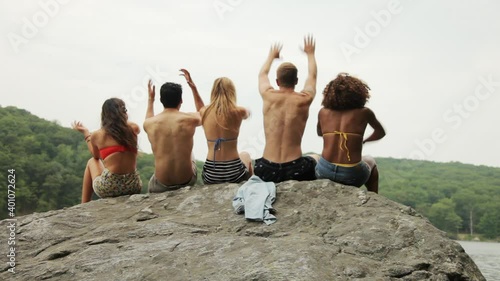 Friends sitting on rock at lake throwing hands in air photo