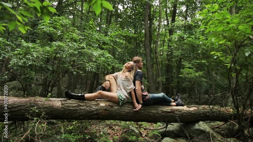 Tilt down to couple sitting back to back holding hands on log in forest photo