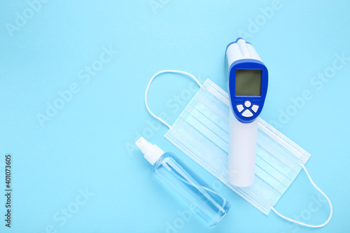 Medical mask, sanitizer bottle and infrared thermometer on blue background