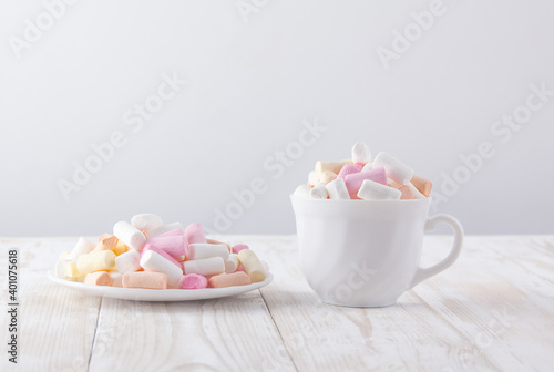 white cup with marshmallows and white saucer with marshmallows on a white wooden table
