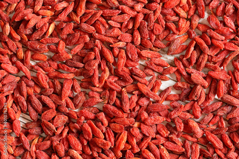 Fototapeta premium Detail closeup photo of goji berry (wolfberry - Lycium chinense) dried fruits heap shot from above, white wooed board visible under