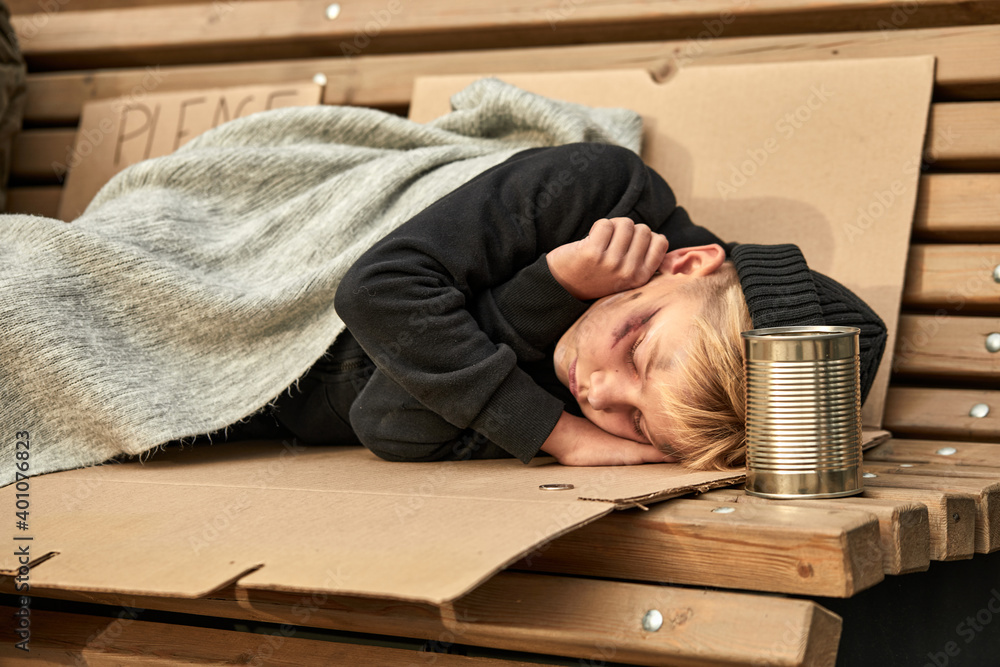 Obraz premium unidentified homeless child begging on street, lying on bench in city streets. Shelter concept.