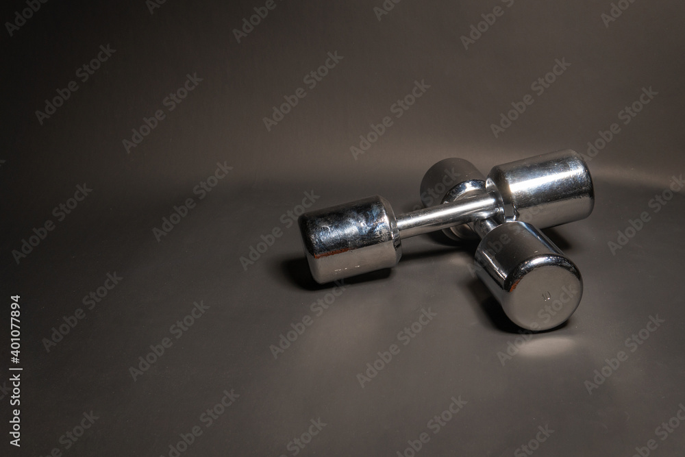 Fitness dumbbells lie, on a black background shine with a metallic color Fitness dumbbells lie, on a black background shine with a metallic color