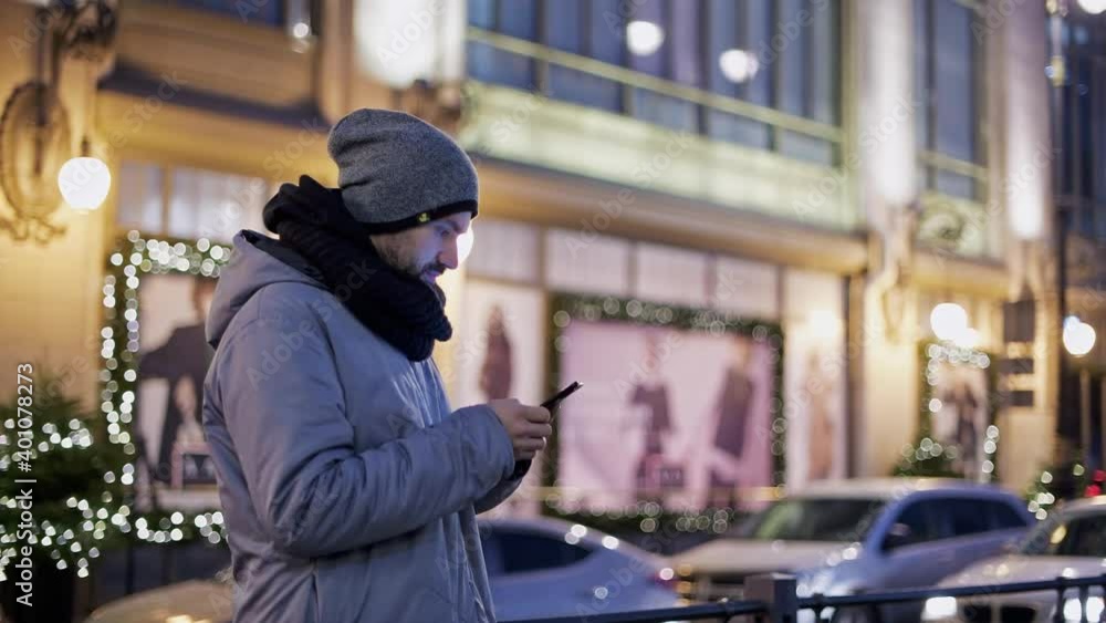 A young man communicates on the phone in the evening in the city. Big city lights. New Year's city. A young man communicates on the phone in the evening in the city. Big city lights. New Year's city.