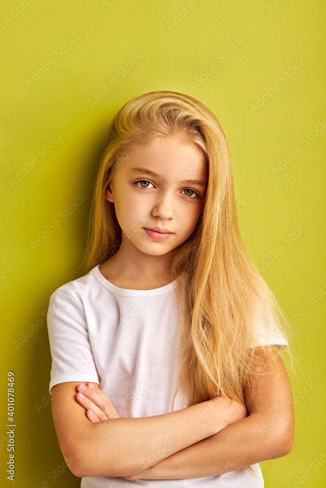 serious child girl with crossed arms looks at camera isolated on green background, having beautiful long hair, wearing white casual t-shirt serious child girl with crossed arms looks at camera isolated on green background, having beautiful long hair, wearing white casual t-shirt