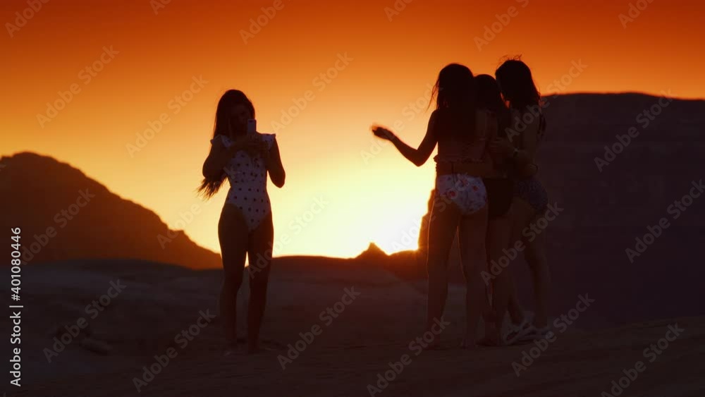 Silhouette of girl photographing friends for cell phone social media at sunset / Glen Canyon National Park, Utah, United States