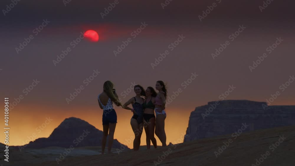 Wide shot of girl photographing friends for cell phone social media at sunset / Glen Canyon National Park, Utah, United States Wide shot of girl photographing friends for cell phone social media at sunset / Glen Canyon National Park, Utah, United States