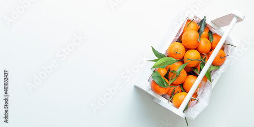 A white basket fresh tangerines with leaves, with white background. Selective focus. View from above. Banner.