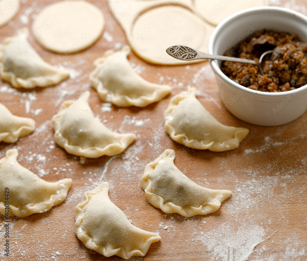 A close-up view of traditional dumplings with vegetarian filling during preparation on a wooden board A close-up view of traditional dumplings with vegetarian filling during preparation on a wooden board