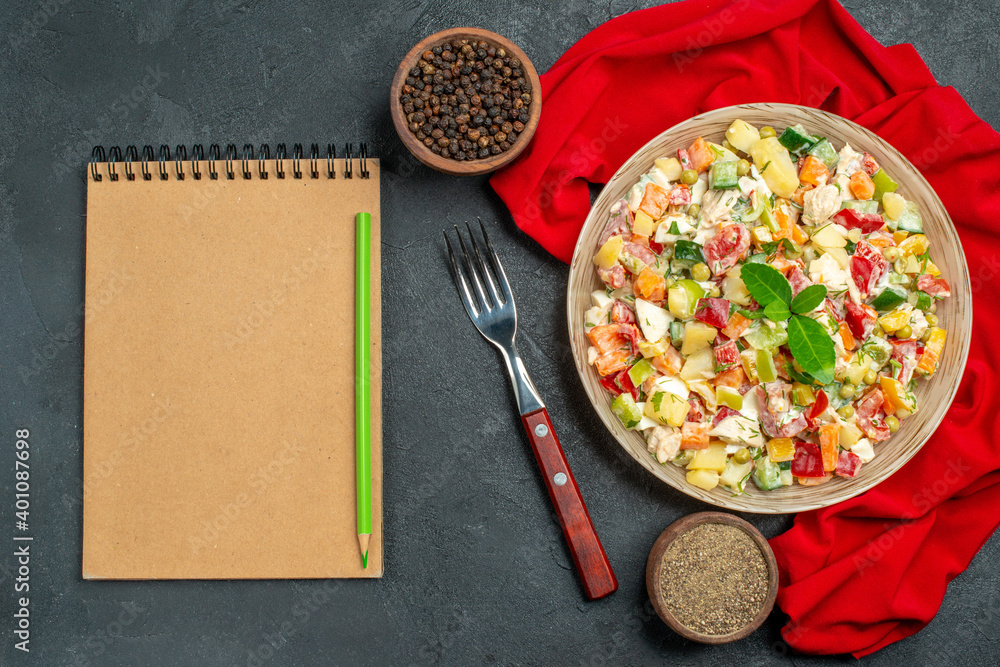 top close view of veggie salad on red napkin with fork notepad and pepper on side on dark grey background