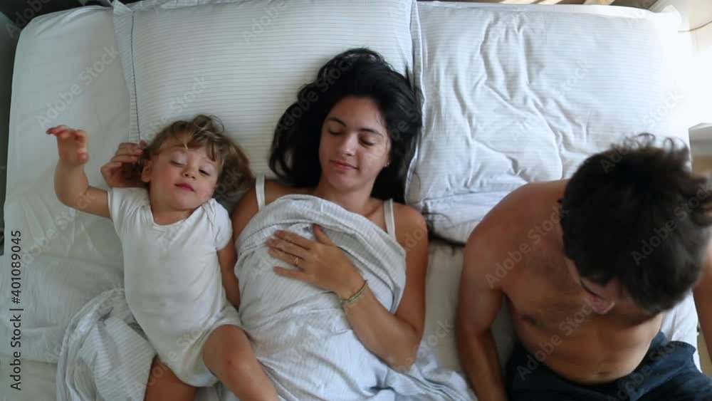 Casual parents in bed with infant baby. Mom and dad in morning bed with toddler. Top view Casual parents in bed with infant baby. Mom and dad in morning bed with toddler. Top view