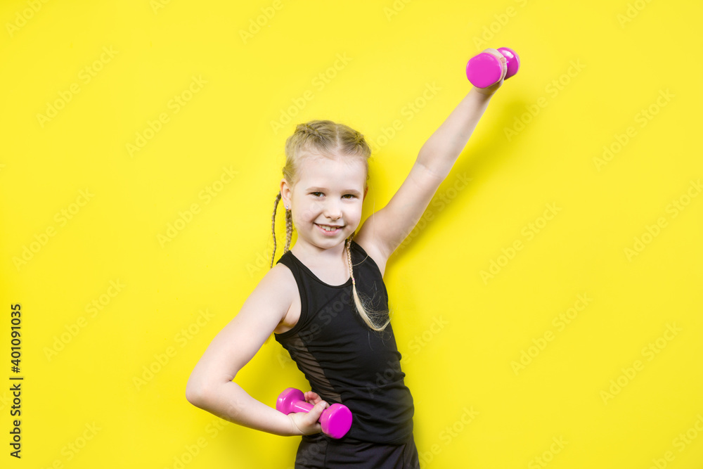 Theme sport and health. Beautiful caucasian child girl with pigtails posing on yellow background with smile. little athlete holding pink dumbbells. Banner for advertising, space for text copy space Theme sport and health. Beautiful caucasian child girl with pigtails posing on yellow background with smile. little athlete holding pink dumbbells. Banner for advertising, space for text copy space