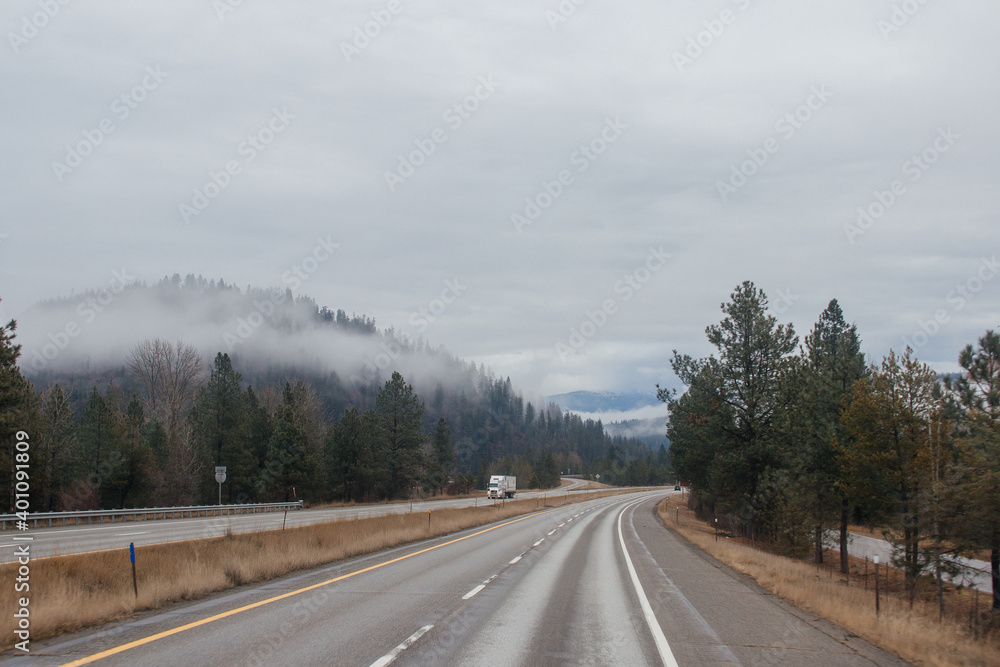 Highway with road signs on the sides among high mountains in the clouds in winter, along which trucks and cars travel. Idaho, USA, 12-5-2020